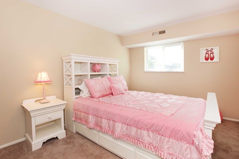 A pink bed with a white nightstand and lamp in a bedroom.