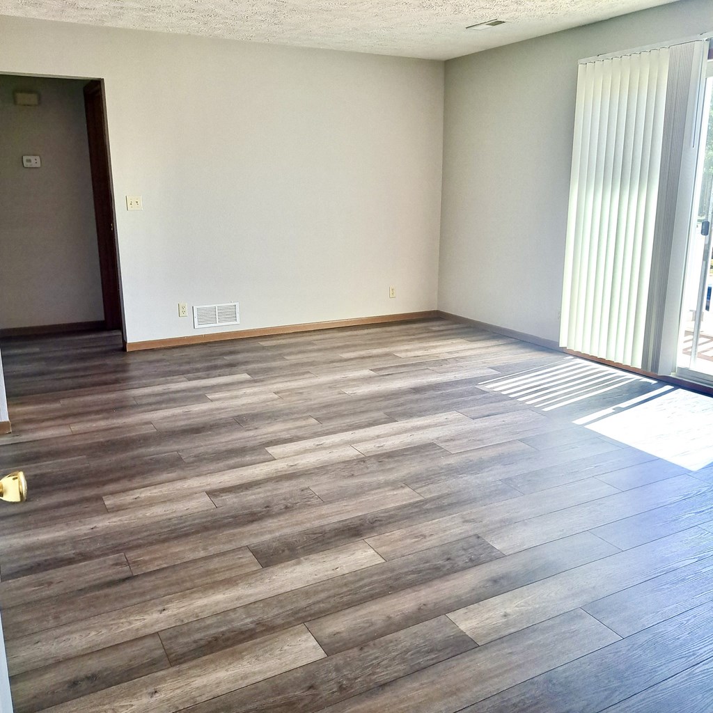an empty living room with wooden floors and a sliding glass door