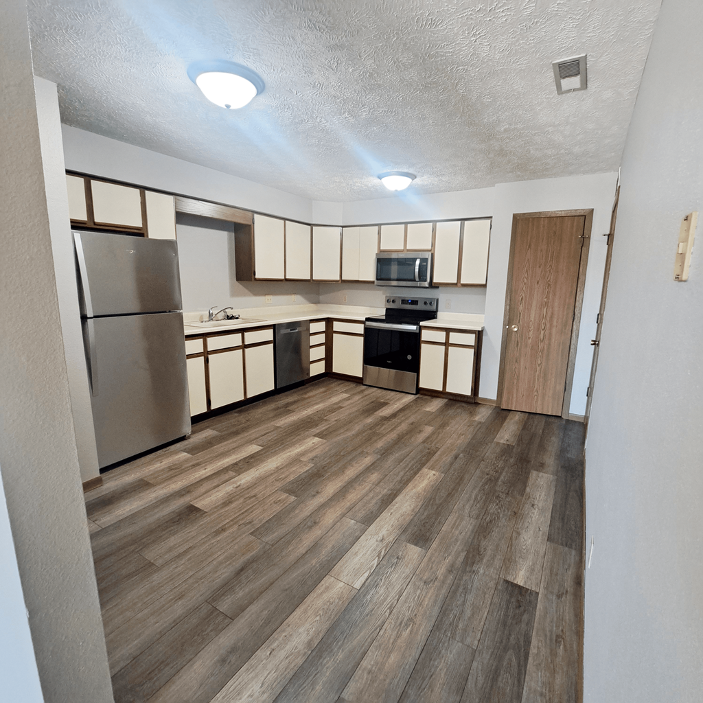an empty kitchen with wood flooring and a stainless steel refrigerator