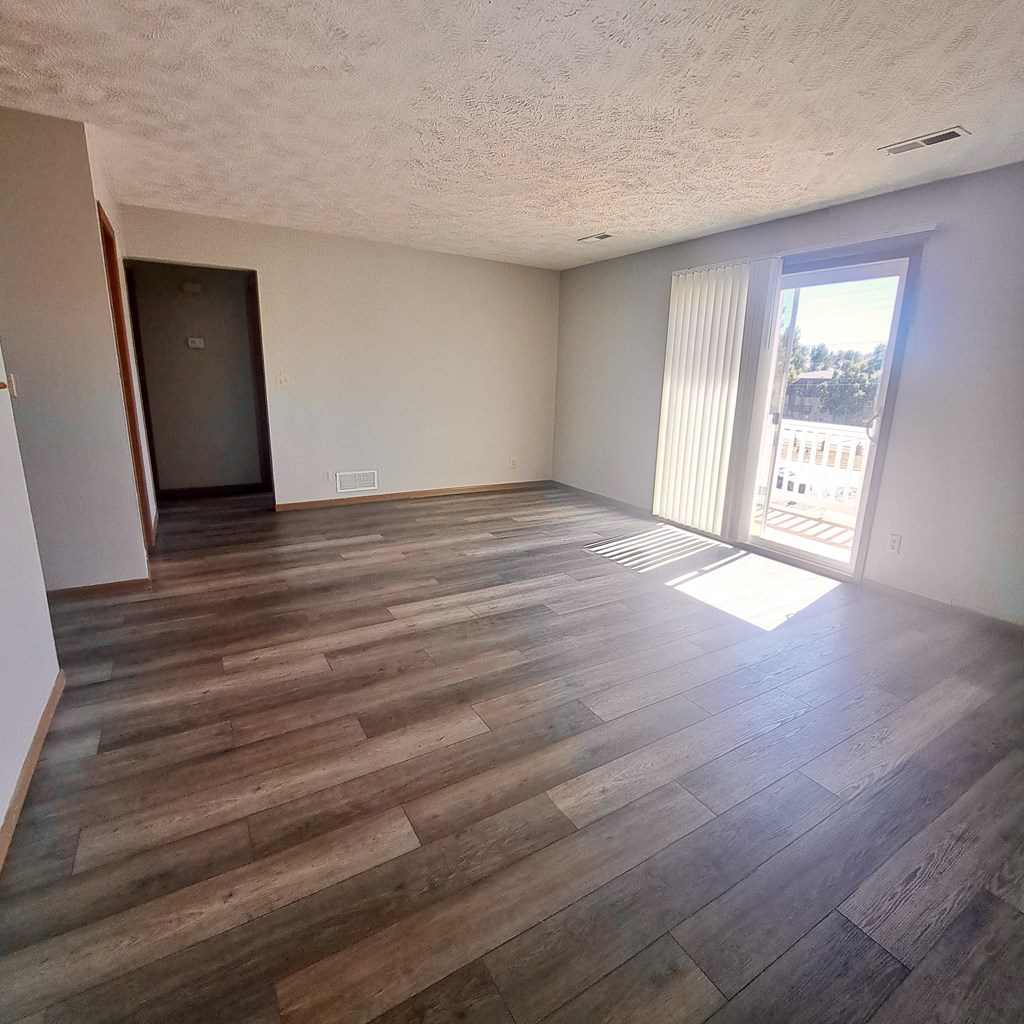 an empty living room with wooden floors and a sliding glass door