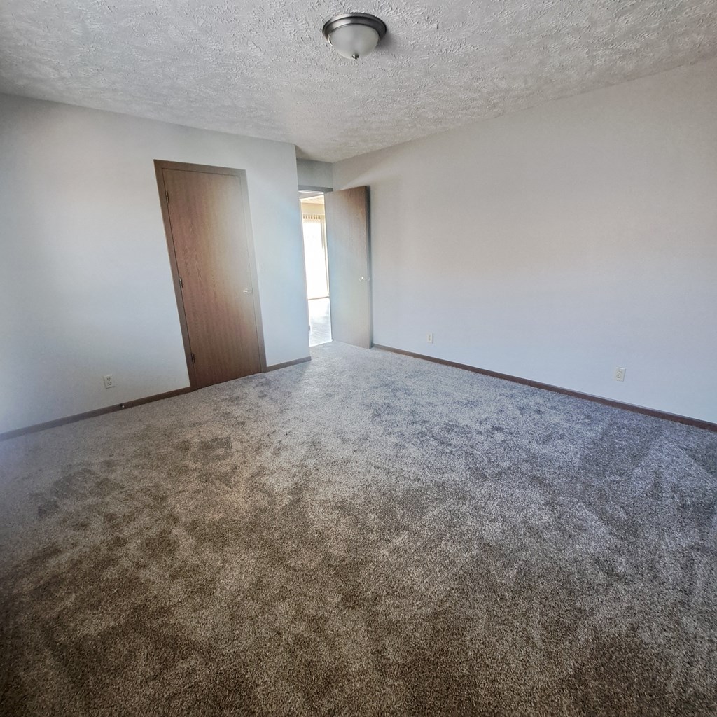 an empty living room with carpet and a door to a bedroom