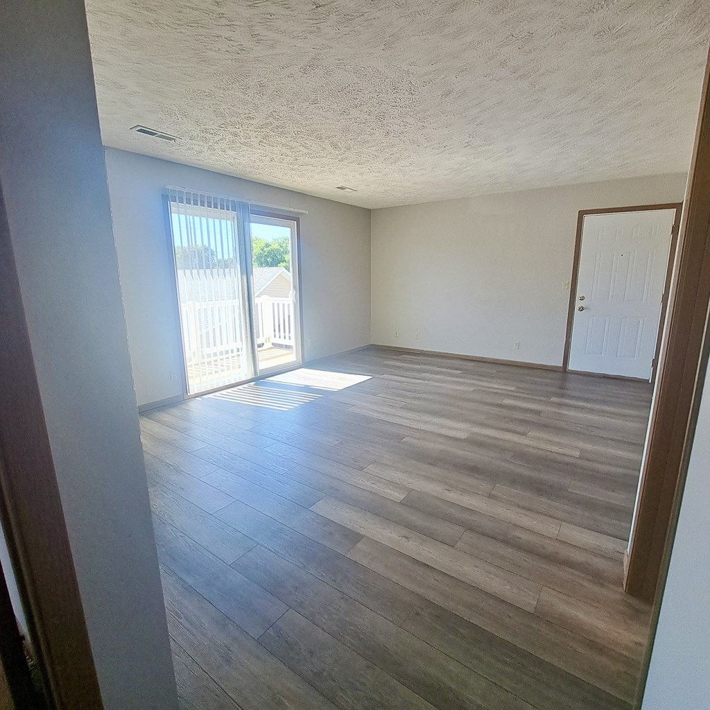 an empty living room with wood flooring and a door to a balcony