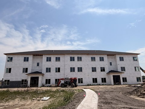 A large white building under construction with a red vehicle in front.