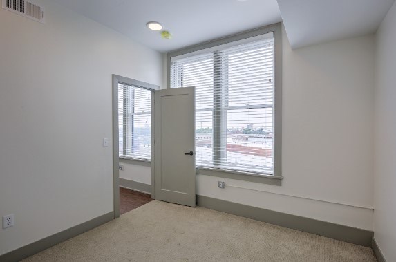 A room with a carpeted floor, a window with blinds, and a door.