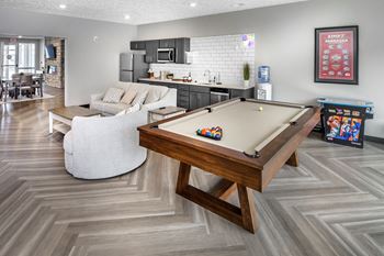 A pool table is in the middle of a room with a white couch and a wooden coffee table.