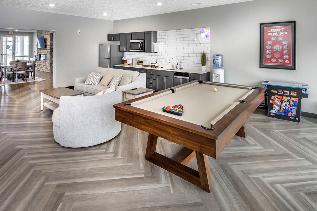 A pool table is in the middle of a room with a white couch and a wooden coffee table.