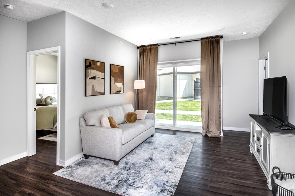 A living room with a grey couch, a television, and a large window with curtains.
