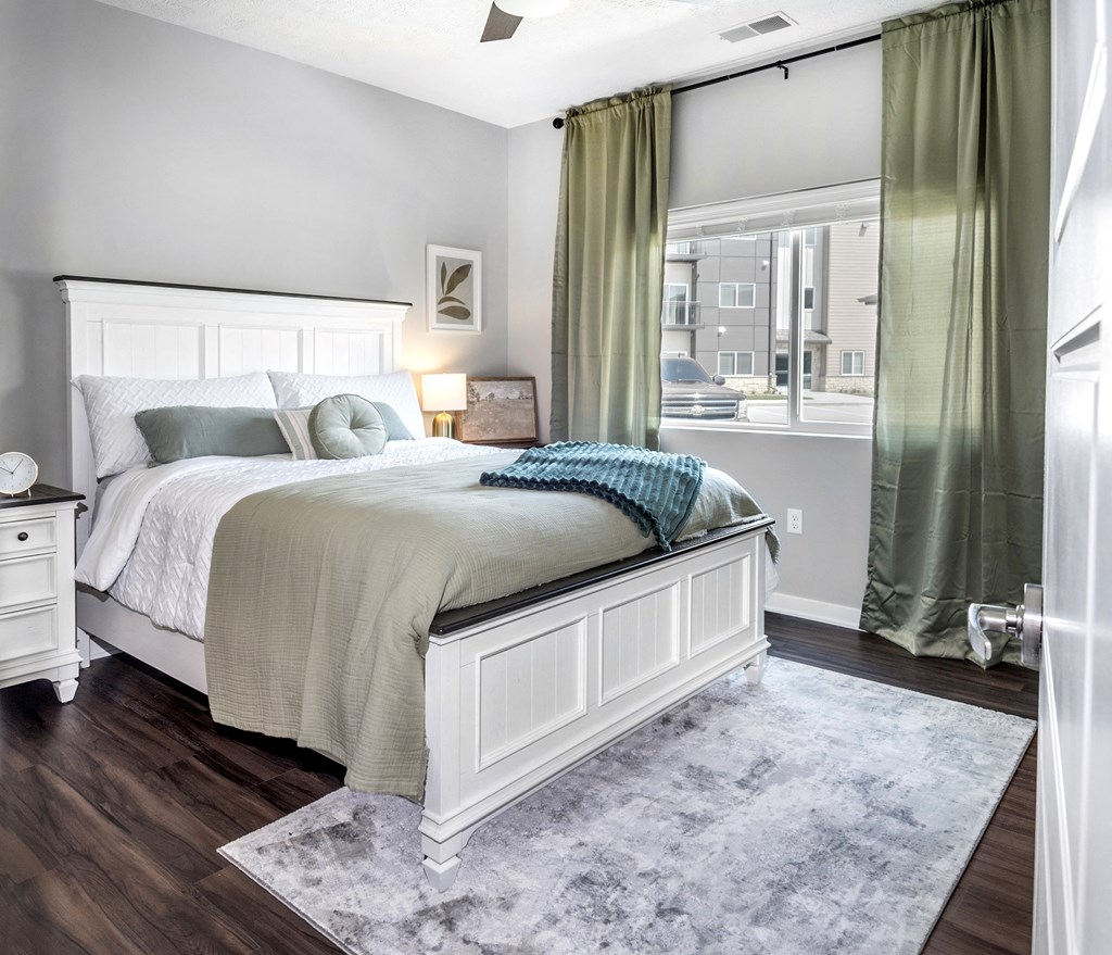 A bedroom with a large bed and a window with green curtains.