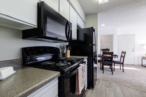 A black stove and refrigerator in a kitchen with a dining table and chairs in the background.