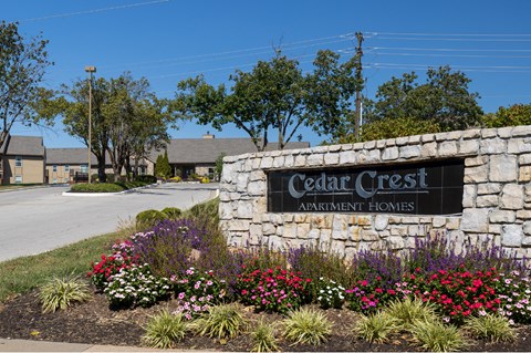The Cedar Crest Apartments sign displayed in front of a stone wall, surrounded by flowers and landscaping.