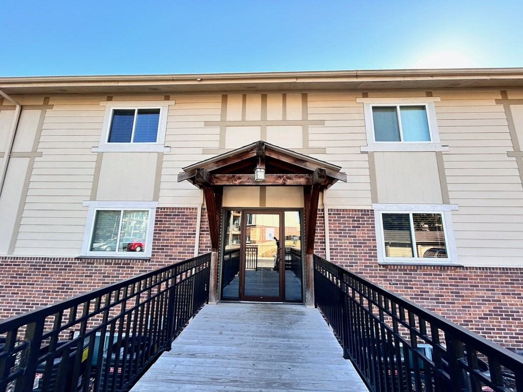 The front entrance of a building with stairs leading up and a brick wall on the side in the Cambridge Apartments complex.