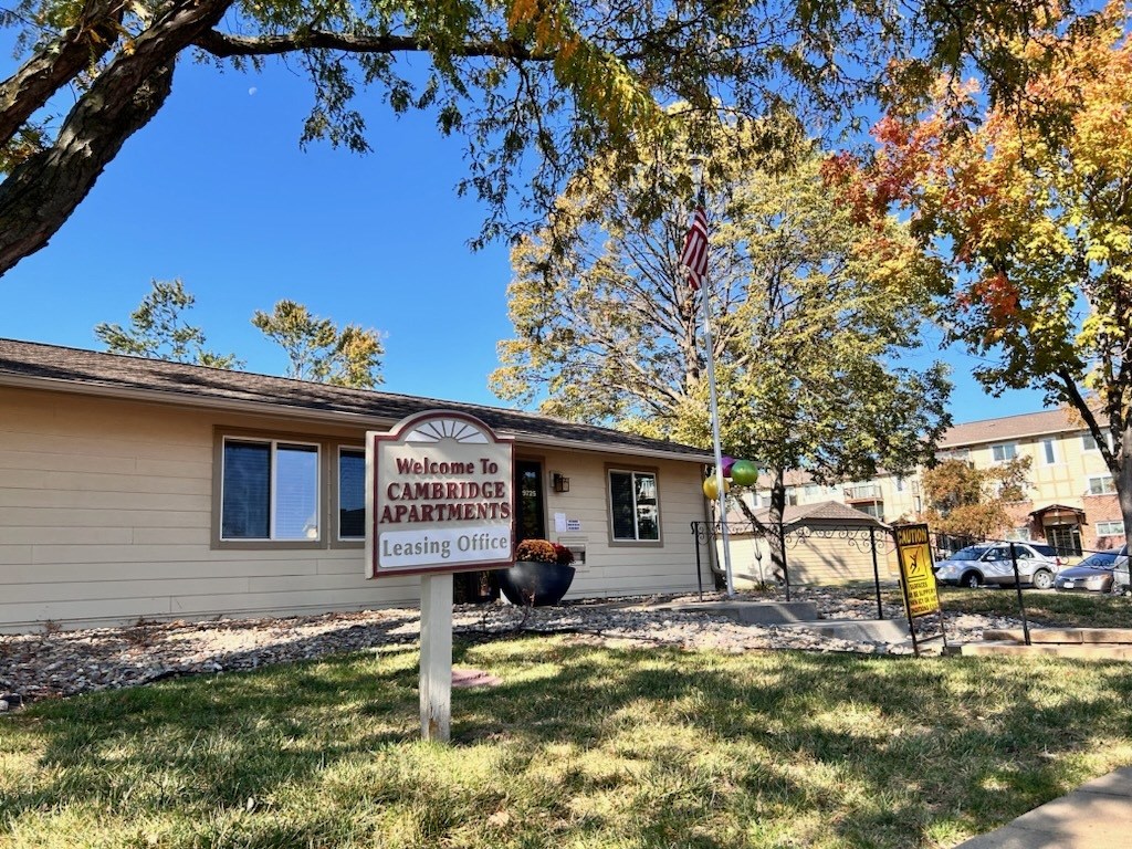 Exterior view of the Cambridge Apartments leasing office with a sign that reads 'Welcome to Cambridge Apartments Leasing Center.