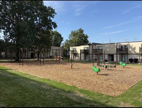 Playground with green swing set and sandbox at Park 25 Apartments surrounded by open outdoor space.