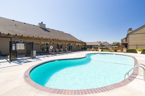 A sparkling swimming pool at Cedar Crest Apartments, surrounded by lounge chairs and lush landscaping.