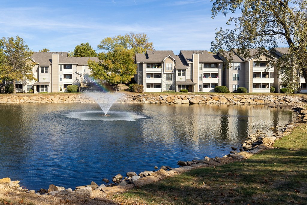 Three Lakes apartment complex showcasing a tranquil lake with a fountain centerpiece and apartment buildings nestled in a serene, green environment.