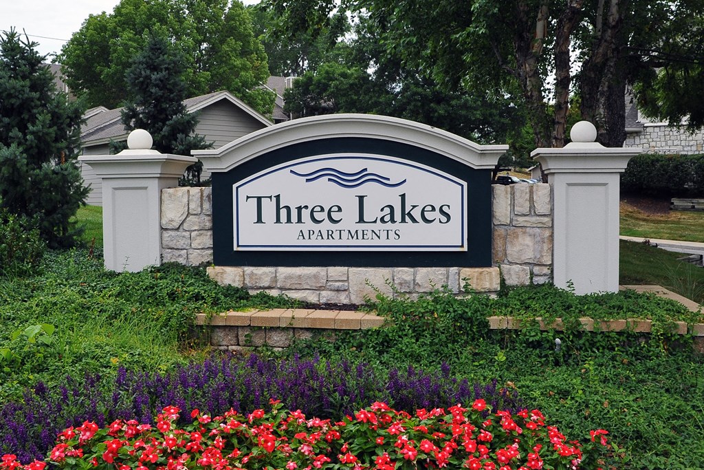 Exterior signage of the Three Lakes apartment complex, prominently displaying the name and surrounded by neatly landscaped greenery.