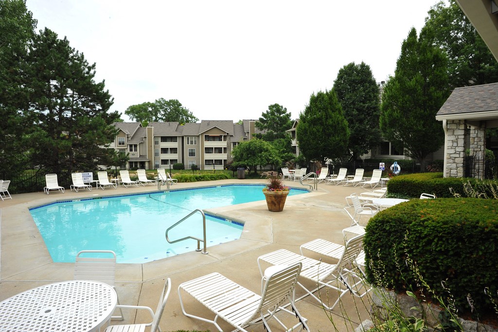 Outdoor swimming pool at Three Lakes Apartments, surrounded by lounge chairs and greenery.