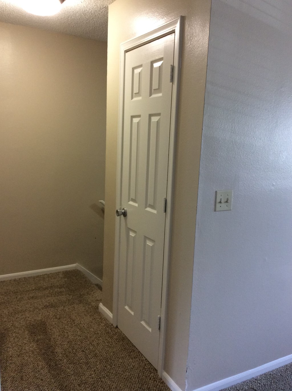 A white door leading to a coat closet in a room with carpeted flooring in the Yeakel Townhome.