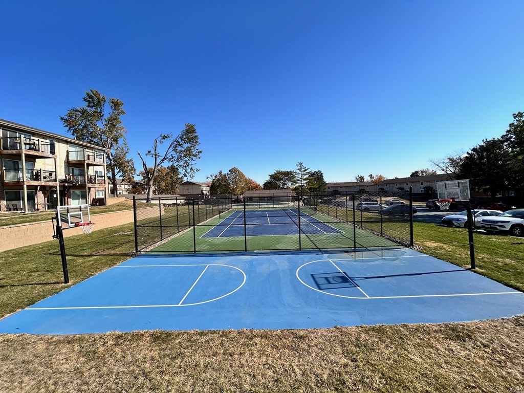 Fenced blue basketball court at Cambridge Apartments, tennis court located behind.