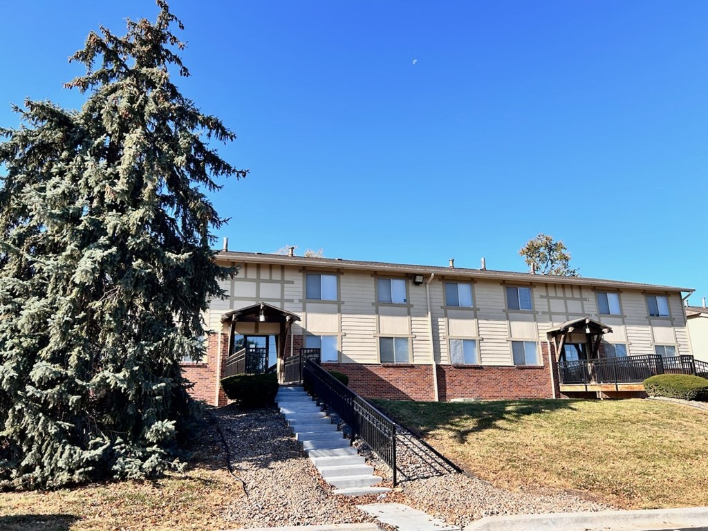 Exterior view of a Cambridge Apartments building with stairs leading to the main entrance and a tree in front.