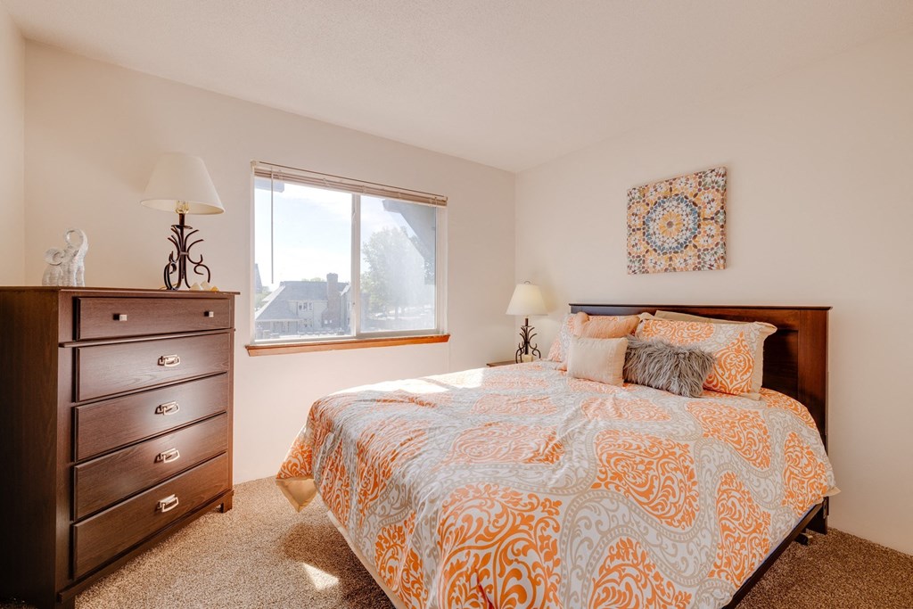 Olde English Village Model Unit - Two Bedroom Bedroom in the two-bedroom model unit at Olde English Village, featuring a comfortable bed and soft lighting.