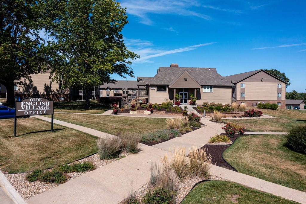 An aerial view of Olde English Village Apartments, nestled among the serene landscape, featuring a cluster of well-maintained buildings with courtyards and walkways.