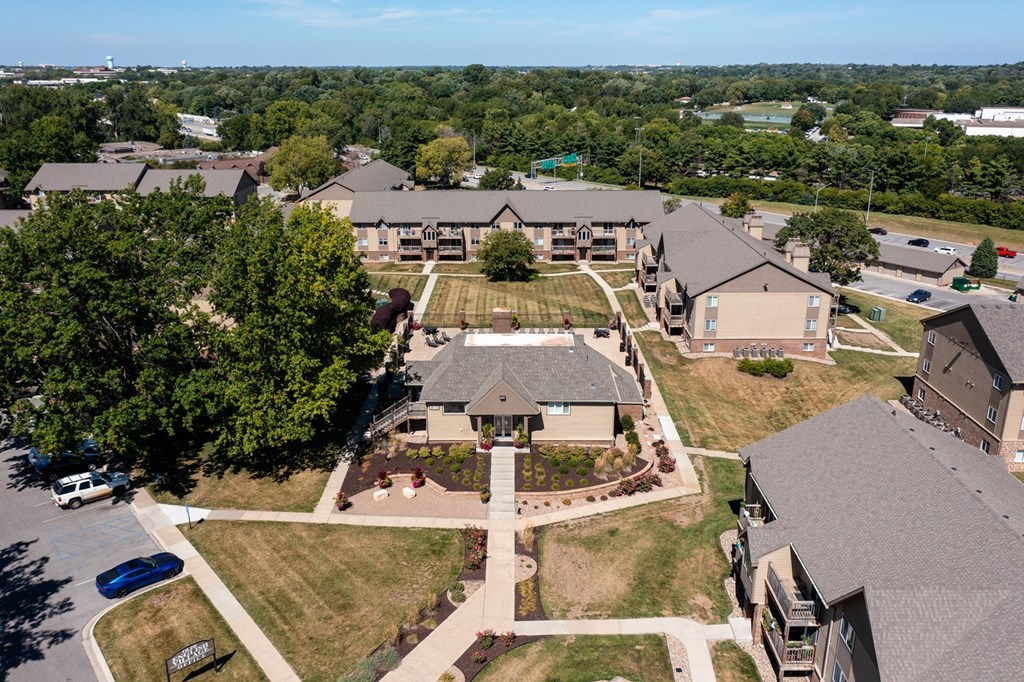 An aerial view of Olde English Village Apartments, nestled among the serene landscape, featuring a cluster of well-maintained buildings with courtyards and walkways.