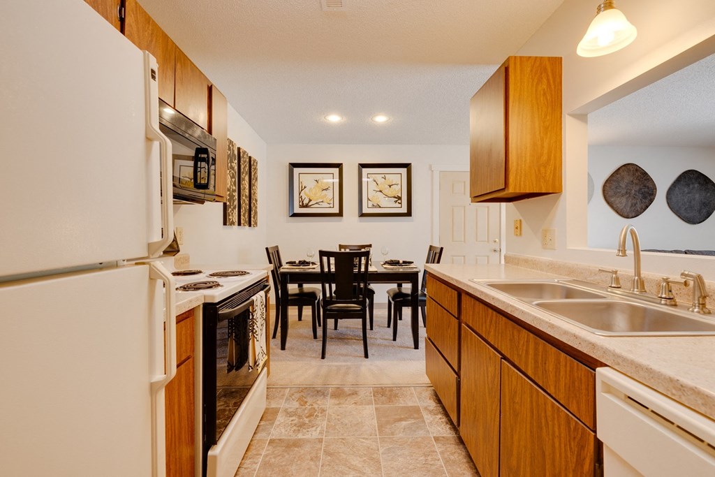 Regency Woods Model Unit - Kitchen Kitchen in a Regency Woods model unit featuring countertops, a refrigerator, and a stove, with a dining area including a table and chairs.