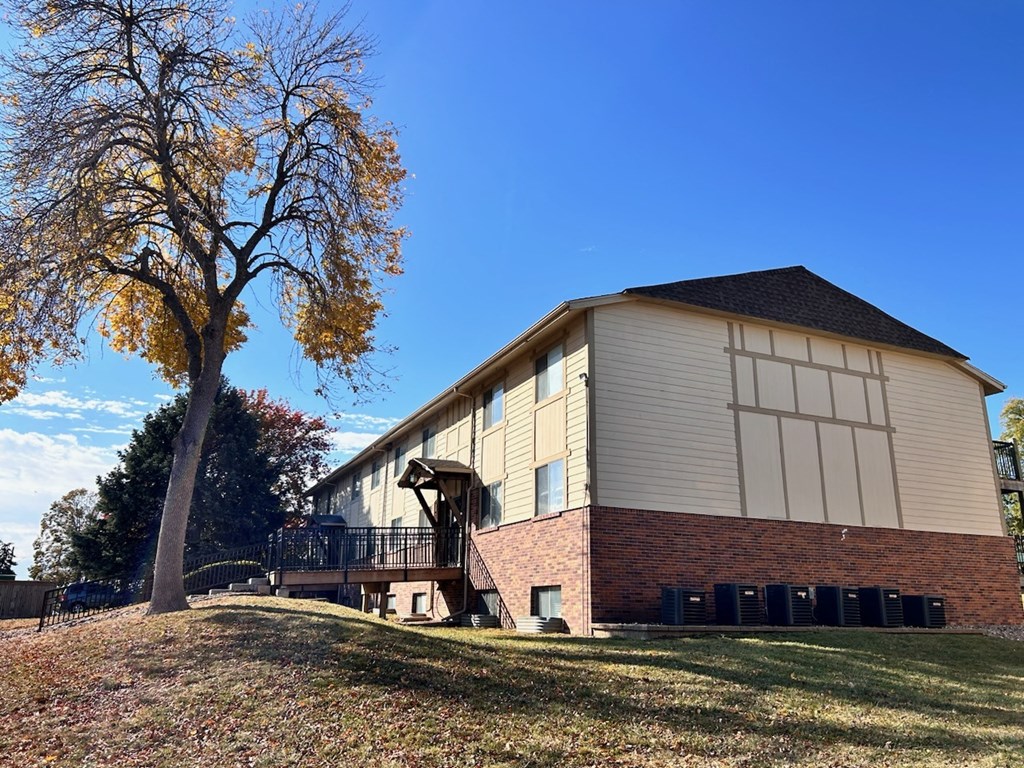 Exterior of an apartment building at Cambridge Apartments, featuring brick on the lower part of the wall and green landscaping.