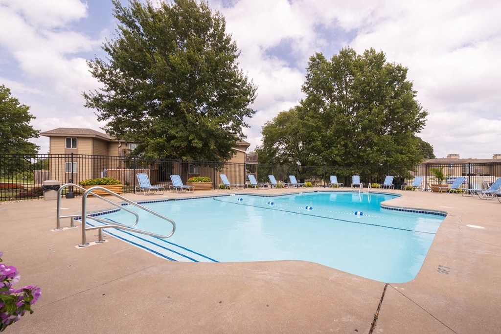 Outdoor swimming pool at Wilshire Apartments complex, surrounded by lounge chairs and landscaped greenery.