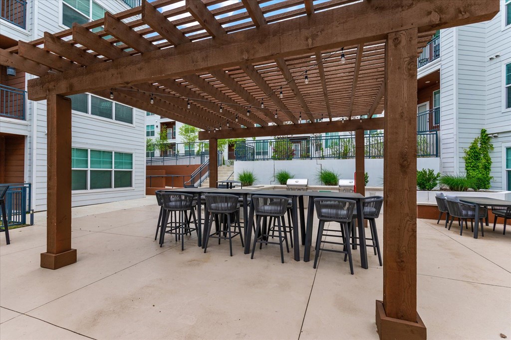 an outdoor patio with a wooden pergola and tables and chairs