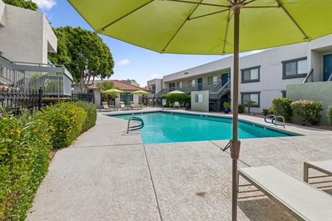 A pool surrounded by a concrete patio and a yellow umbrella.