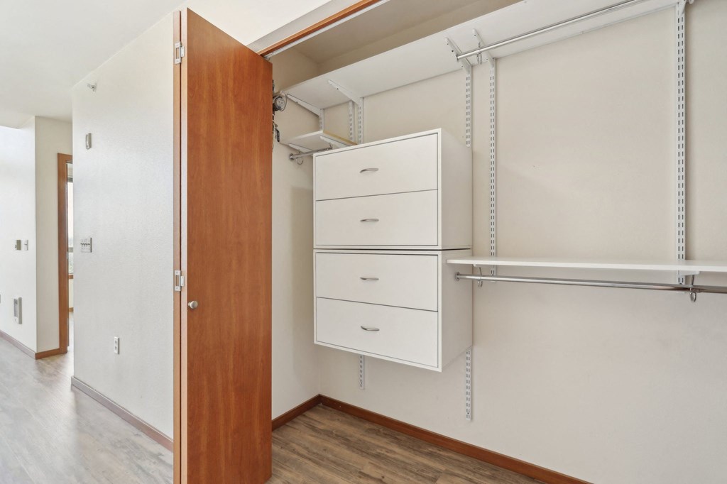 A white cabinet with three drawers is open to a room with a white wall and a brown door.