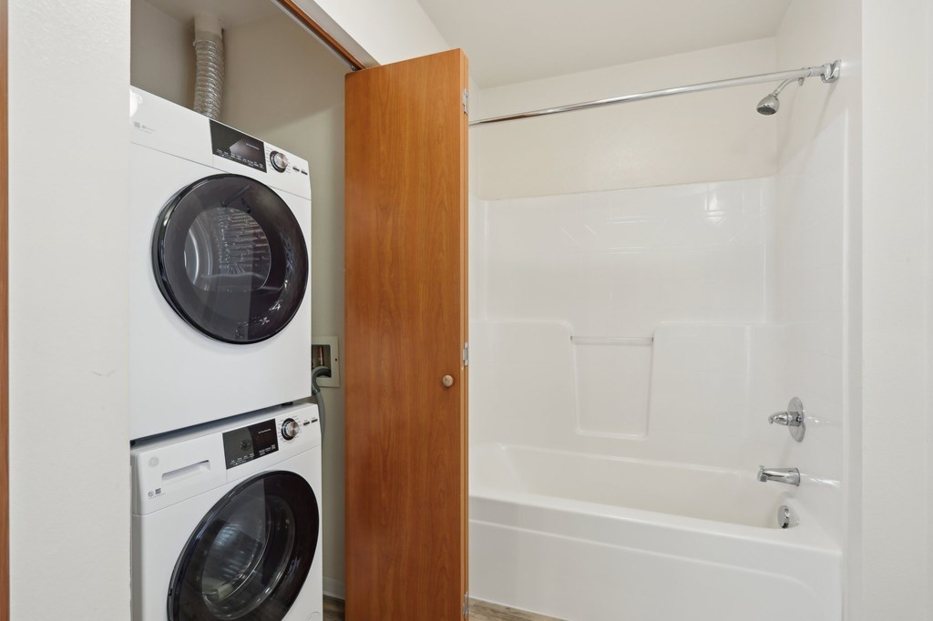 A white washing machine and dryer are in a small laundry room with a wooden door.
