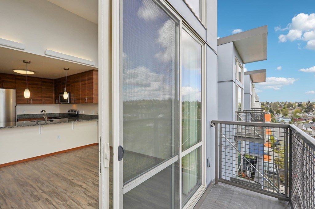 A balcony with a glass door leading to a room with wooden floors and a brick wall.