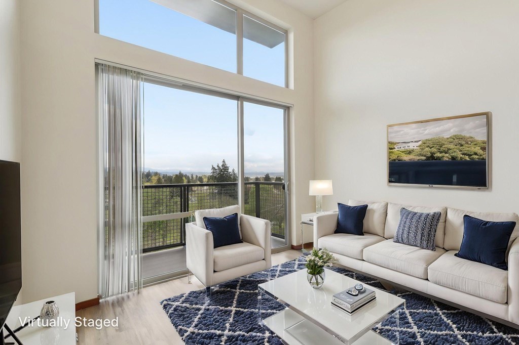 A living room with a white couch, a coffee table, and a large window with a view of the outside.