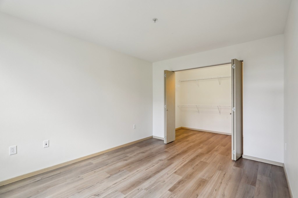 A room with a white wall and a wooden floor with a door open.