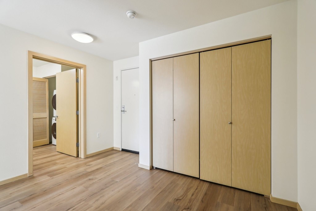 A room with wooden floors and a white wall with a mirror and a wardrobe.