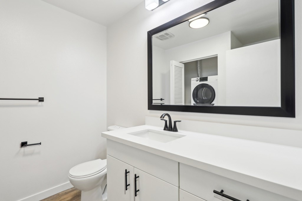 A bathroom with a white countertop and a mirror reflecting a fan.