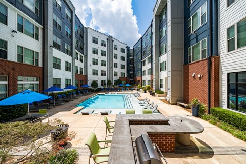 an outdoor pool with lounge chairs and umbrellas in front of an apartment building