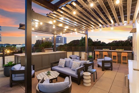 a roof deck with couches and chairs and a bar with a sunset