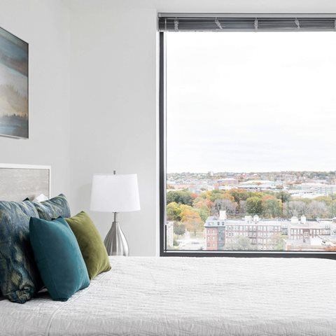 A bedroom with a large bed and a view of a cityscape through a window.