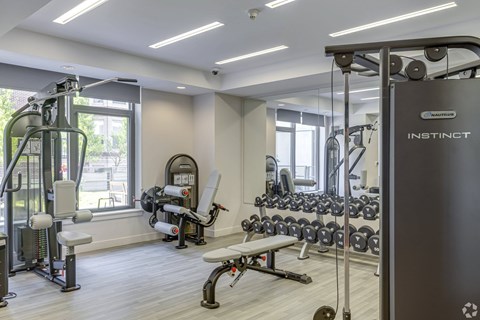 A gym with a variety of equipment including a weight bench, a leg press machine, and a cable machine.