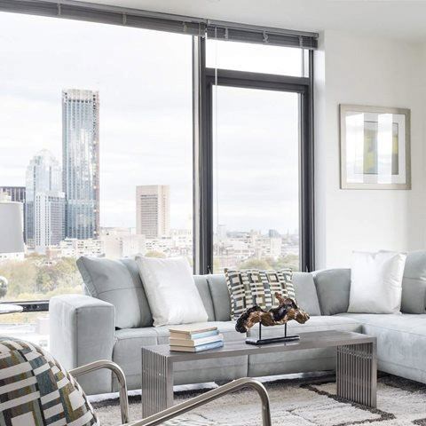 A living room with a grey couch and a city view through the window.