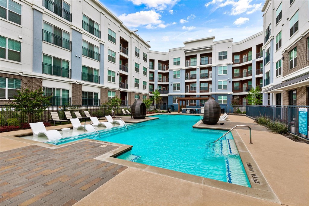 a swimming pool with lounge chairs and a water feature in front of an apartment building