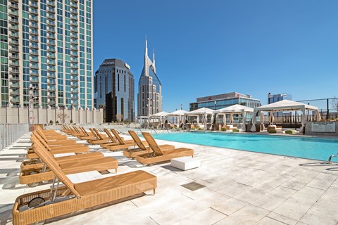 A pool with sun loungers in front of a city skyline.