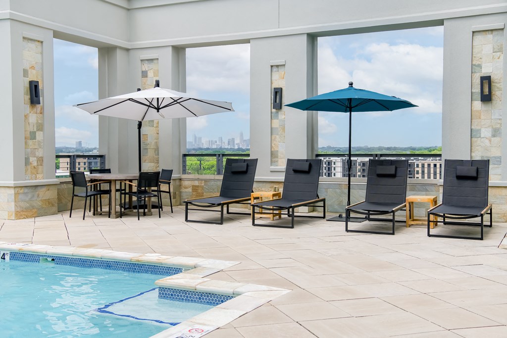 a pool area with lounge chairs and umbrellas and a view of the city