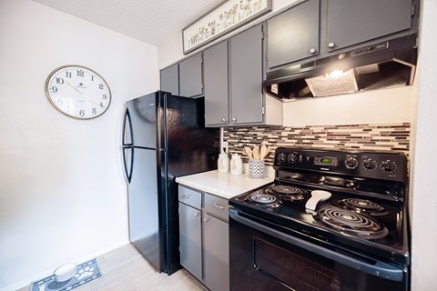 A black refrigerator is in a kitchen next to a stove.
