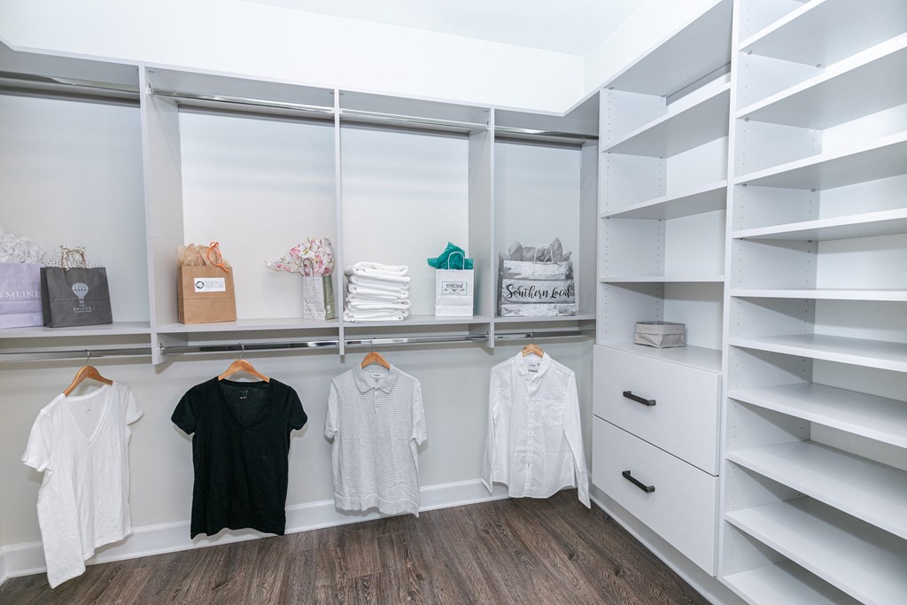 a walk in closet with white shelves and a window