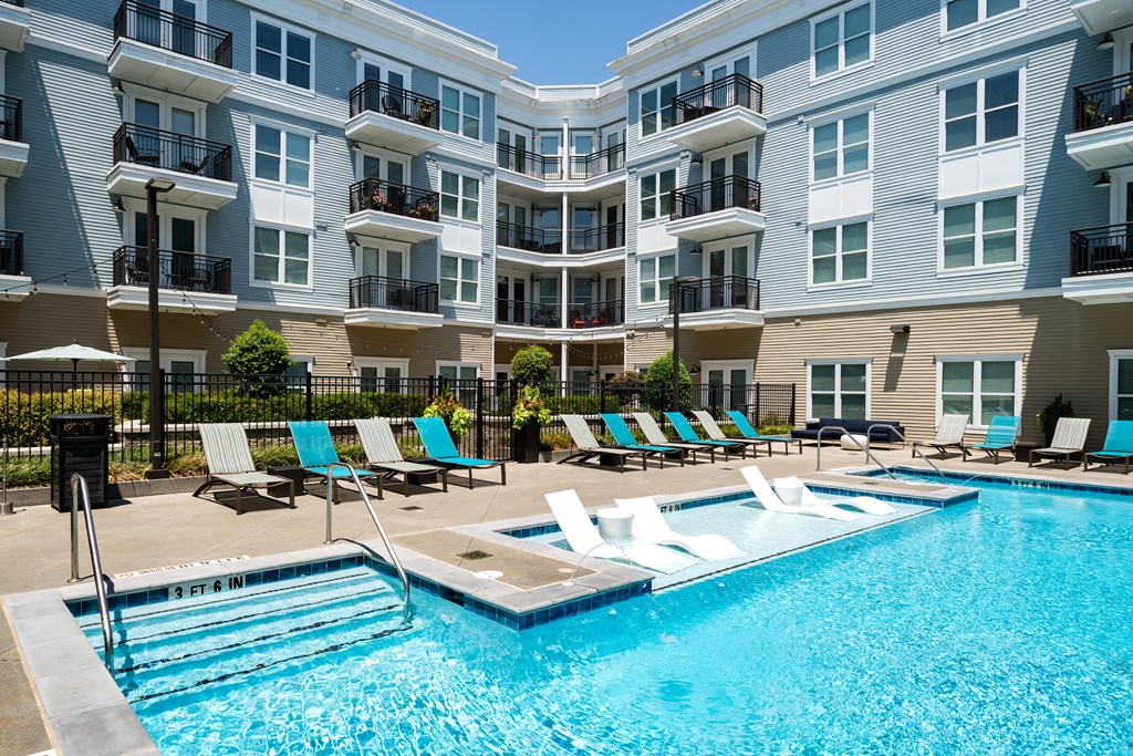 a swimming pool with lounge chairs in front of an apartment building